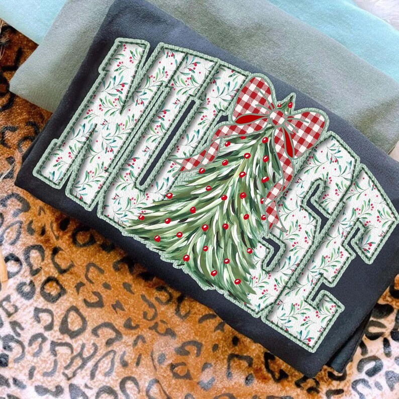 Op de afbeelding: Een zwart sweatshirt met het woord "MERRY" in een wit bloemenpatroon met groene randen. Een kerstboomontwerp met rode bessen en een rood-witte geruite strik staat rechts. Twee andere sweatshirts zijn op de achtergrond te zien.