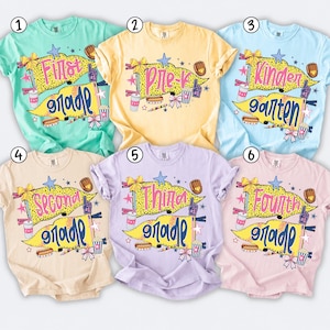 May include: Six short-sleeved t-shirts in mint, yellow, light blue, beige, lavender, and light pink. Each shirt features a graphic of two yellow pennants with the text First Grade, Pre-K, Kindergarten, Second Grade, Third Grade, and Fourth Grade.
