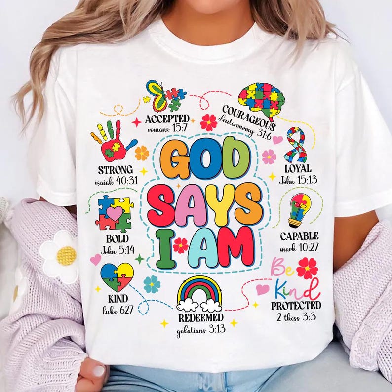 May include: White t-shirt with a colorful graphic design that says "God Says I Am" with bible verses and illustrations. The design includes a rainbow, a heart, a lightbulb, and a hand.