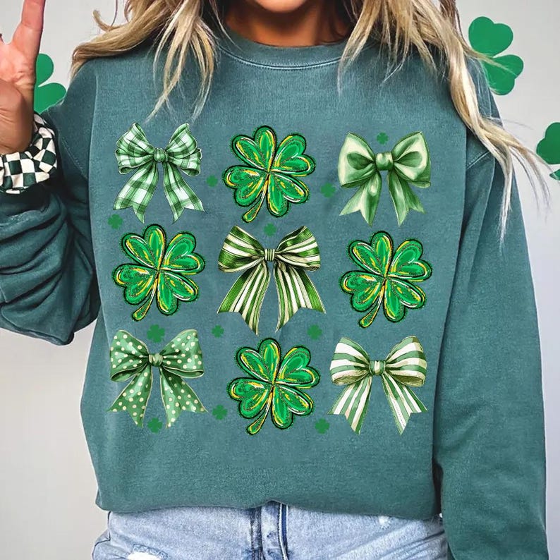 May include: Teal green sweatshirt with a graphic print of green four-leaf clovers and green bows.