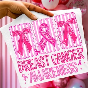 May include: White t-shirt with pink graphics promoting Breast Cancer Awareness. The design includes pink ribbons and bows within decorative frames, and the words "BREAST CANCER AWARENESS" in a playful font.