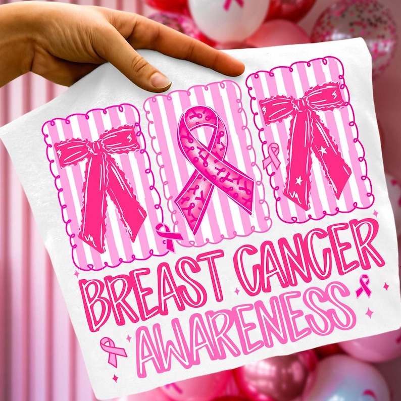 May include: White t-shirt with pink graphics promoting Breast Cancer Awareness. The design includes pink ribbons and bows within decorative frames, and the words "BREAST CANCER AWARENESS" in a playful font.