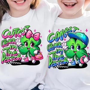 May include: Two white t-shirts with a green four-leaf clover cartoon character. One shirt says "Cutest clover in the patch" with a pink bow on the clover. The other shirt says "Coolest clover in the patch" with a blue baseball cap on the clover.