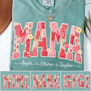 Op de afbeelding: Een tealkleurig T-shirt met het woord "MAMA" in een patchwork-ontwerp van rode en roze stoffen, versierd met madeliefjes en aardbeien. De namen "Layla", "Oliver" en "Taylor" staan eronder.