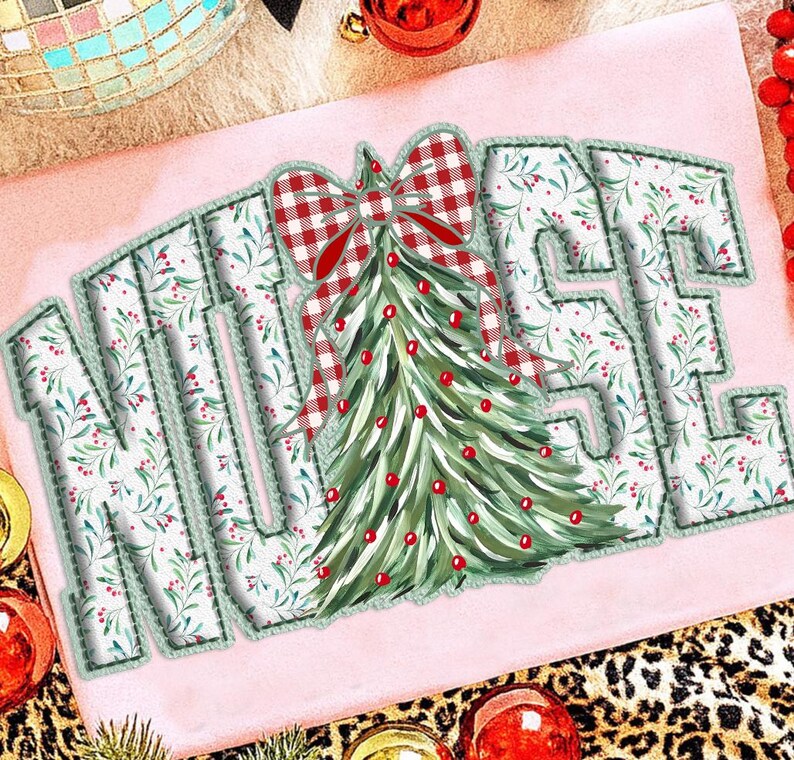 Op de afbeelding: Lichtroze t-shirt met het woord "NURSE" in een decoratief lettertype. De letters zijn wit met een groen bloemenpatroon en een groen gestikte rand. Een kerstboom en een rood geruite strik staan in het midden.