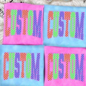 May include: Four t-shirts, two pink and two light blue, each with the word "CUSTOM" in a colorful checkered pattern. The shirts are arranged on a white, fluffy surface with disco balls and a pearl necklace.