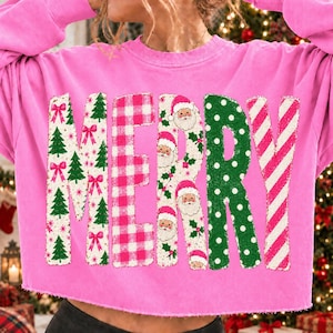 May include: A bright pink long-sleeve sweatshirt featuring the word MERRY in large letters. Each letter has a distinct pattern: M has green trees and pink bows, E has a pink plaid, R has Santa faces, R has green polka dots, and Y has red stripes.