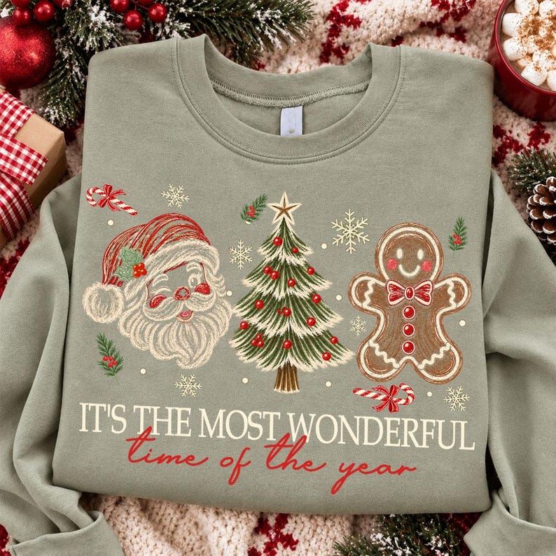 K&ouml;nnte beinhalten: Ein salbeigr&uuml;nes Sweatshirt mit Rundhalsausschnitt und einem Grafikdruck von Weihnachtsmann, geschm&uuml;cktem Weihnachtsbaum und Lebkuchenmann. Der Text "IT'S THE MOST WONDERFUL time of the year" ist in wei&szlig;er und roter Schrift darunter gedruckt.