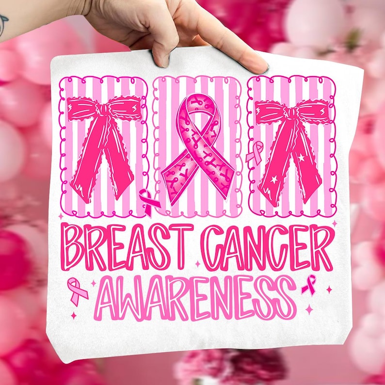 May include: White tote bag with a pink Breast Cancer Awareness design. The design includes pink ribbons, bows, and the words "Breast Cancer Awareness" in a decorative font. The background features pink and white stripes.