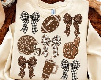 May include: A cream-colored crewneck sweatshirt featuring a graphic print of four decorative bows in black and white gingham or brown polka dot patterns, a brown football, a leopard print football helmet, a foam finger with #1, and a tumbler.