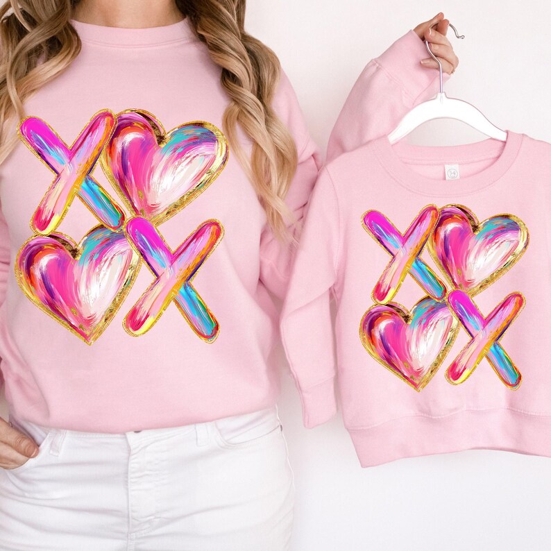 Puede incluir: Sudaderas rosas con un gr&aacute;fico de dos corazones y un dise&ntilde;o 'XO' en pinceladas coloridas con detalles dorados.