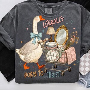 May include: Dark gray sweatshirt with a whimsical graphic of a goose pushing a shopping cart filled with vintage items. The text reads "Literally Born to Thrift". The goose wears a blue bow tie and has orange feet.
