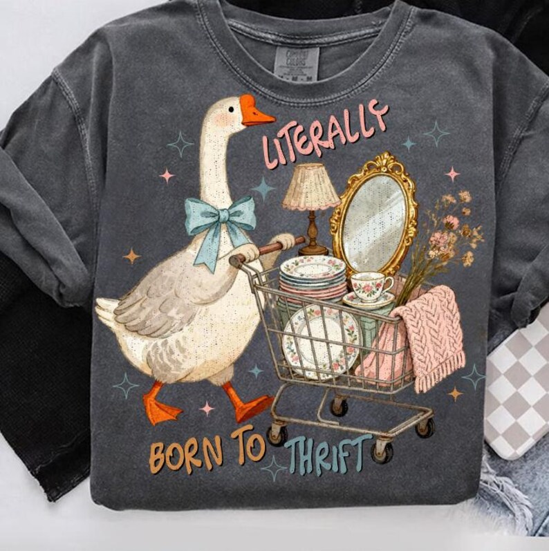 May include: Dark gray sweatshirt with a whimsical graphic of a goose pushing a shopping cart filled with vintage items. The text reads "Literally Born to Thrift". The goose wears a blue bow tie and has orange feet.