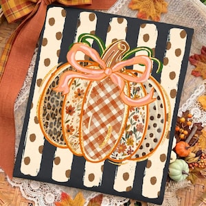 May include: A rectangular sign featuring a central pumpkin illustration with segments of leopard print, floral patterns, and orange gingham. A light pink bow sits atop the pumpkin, set against a black and cream vertical striped background with dots.