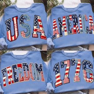 May include: Four light blue sweatshirts with patriotic designs. One says "USA", another "AMERICA", a third "FREEDOM", and the last "1776". The lettering is made of red, white, and blue fabric in a patchwork style, evoking the American flag.