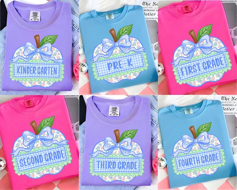 Op de afbeelding: Een collectie van zes T-shirts met ronde hals in lavendel, lichtblauw en felroze. Elk shirt heeft een centrale appelafbeelding met een blauwe strik, een groen blad en een geruit lint met de leerjaren van de kleuterschool tot de vierde klas.