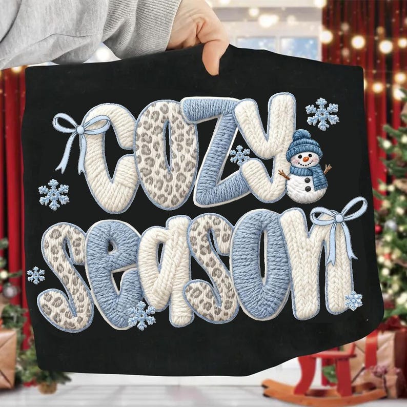 Pu&ograve; includere: Borsa tote nera con la scritta "COZY SEASON" in un carattere a maglia. Le lettere hanno un motivo leopardato, accenti bianchi e azzurri. Include fiocchi di neve e un pupazzo di neve.