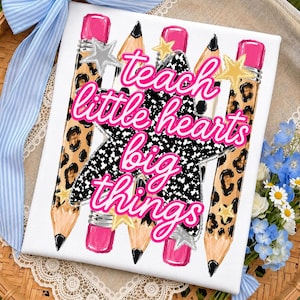 Op de afbeelding: Een vierkant wit canvas met een centraal zwart-wit gespikkeld stergrafiek met de roze tekst "teach little hearts big things" eroverheen. Het ontwerp bevat vier potloden met luipaardprint en roze gummen, plus kleine gouden en zilveren sterren.