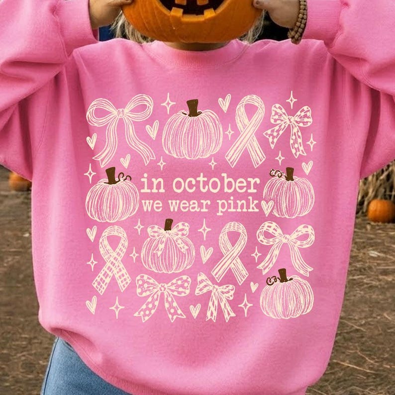 May include: A bright pink sweatshirt featuring a white graphic print of pumpkins, ribbons, and hearts. The text in the center reads, in october we wear pink. The design includes various styles of bows and pumpkins arranged in a grid-like pattern.