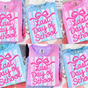 May include: A collection of pastel-colored t-shirts with the text "Last Day of School" in a pink, glittery font. The shirts feature a bow and striped design. Colors include pink, blue, and purple.