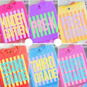 May include: A collection of colorful t-shirts, each featuring a grade level design. The shirts are in various colors, including pink, purple, yellow, orange, blue, and pink. Each shirt has a vertical striped pattern and the grade level printed in a bold font.