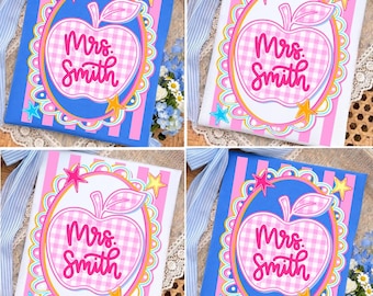 May include: Four images of a notebook with a pink and white gingham apple design. The apple is surrounded by a scalloped border and stars. The text "Mrs. Smith" is written in pink script. The background is striped.