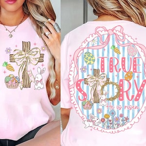 Op de afbeelding: Roze T-shirt met een Paasontwerp. Het ontwerp bevat een houten kruis met een strik, een konijn, paaseieren en de woorden "TRUE STORY" en "He is risen". De achterkant van het shirt heeft een vergelijkbaar ontwerp.
