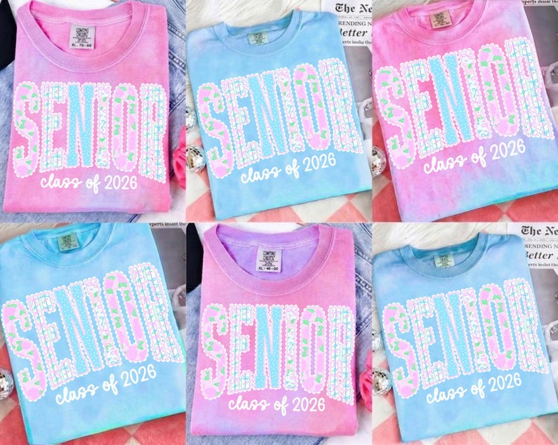 May include: Tie-dye t-shirts in shades of pink, blue, and purple. Each shirt features the word "SENIOR" in large, floral-patterned letters, with "class of 2026" below. The shirts are casual and suitable for graduation.