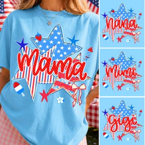 Puede incluir: Camiseta azul claro con un diseño patriótico de estrella. El gráfico incluye la palabra "Mama" en escritura roja, rodeada de estrellas, rayas y otros elementos festivos. También se muestran diseños adicionales con "Nana", "Mimi" y "Gigi".