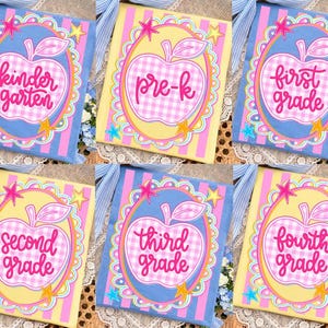 May include: A collection of six decorative school-themed books. Each book features a large apple design with the grade level written inside. The books are in various colors, including blue, yellow, and pink, with star accents.