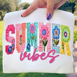 Puede incluir: Camiseta blanca con la frase bordada "SUMMER VIBES" en letras coloridas con temática floral. Las letras son rosas, naranjas, turquesas, azules y verdes, con patrones florales y cuadros. La palabra "vibes" está en rosa cursiva.