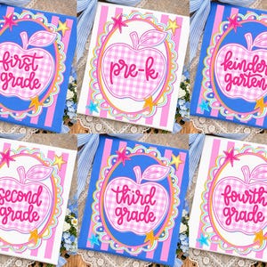 May include: A collection of six school-themed canvases. Each canvas features an apple design with grade level text: "first grade", "pre-k", "kindergarten", "second grade", "third grade", and "fourth grade". The backgrounds are striped in pink and white or blue and pink.