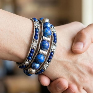Peut inclure: Bracelet enroulé avec des perles de lapis-lazuli bleues et des détails argentés. Le bracelet est enroulé autour du poignet avec une lanière en cuir. Le design comprend des perles rondes plus grandes et des perles plus petites.
