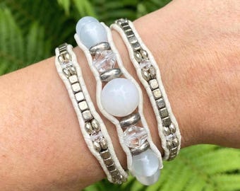 May include: Three wrap bracelets with white leather, silver-tone metal accents, and light blue and white beads. The bracelets are stacked on a wrist, showcasing the design and materials.