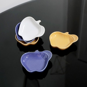 May include: Three ceramic apple-shaped dishes in white, yellow, and purple.