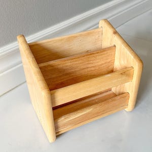 May include: A light-colored wooden desk organizer with three compartments. The organizer is made of natural wood and has a simple, rectangular design. The compartments are separated by horizontal dividers.