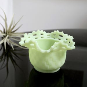 Könnte beinhalten: Eine kleine, hellgrüne Glasschale mit einem gewellten, spitzgeformten Rand. Die Schale ist aus Milchglas und hat einen Vintage-Look.