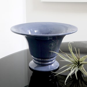 May include: A blue ceramic vase with a wide, flared opening and a pedestal base. The vase is sitting on a black surface.