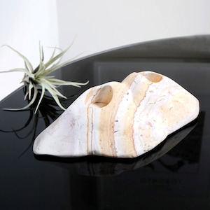 May include: A white and brown stone candle holder with two holes for candles. The holder is shaped like a rock and has a natural, organic look.