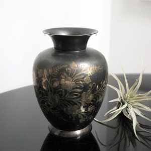 Könnte beinhalten: Eine schwarze Vase mit goldenen Blumenmustern. Die Vase hat eine breite Öffnung und einen runden Körper.