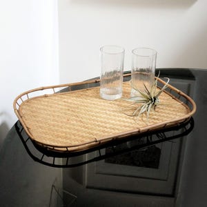 May include: A woven wicker tray with a natural brown finish and a rectangular shape. Two clear glass tumblers and a small green plant are on the tray.