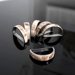 May include: Set of seven silver napkin rings with a bone inlay design. The rings are arranged in a semi-circle on a black surface.