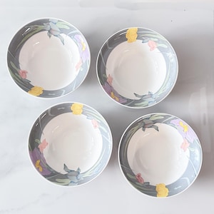 Può includere: Un set di quattro ciotole rotonde in ceramica con interno bianco e un ampio bordo grigio decorato con un motivo floreale di fiori gialli, rosa e viola con foglie verdi. Le ciotole sono disposte in formazione quadrata, viste dall'alto.