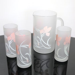May include: A set of four frosted glass tumblers and a pitcher with a floral design. The glasses and pitcher are frosted white with a pink floral pattern.