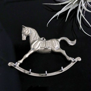 May include: A silver rocking horse key holder with five hooks. The horse is in a galloping pose with a saddle and stirrups.