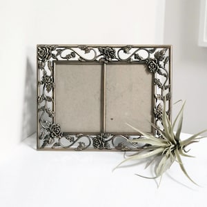 May include: A silver-toned picture frame with a double opening and a floral design. The frame is decorated with roses and vines.