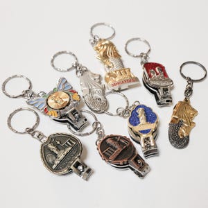 May include: A selection of keyrings with diverse designs, including the Merlion statue, in gold, silver, red, and blue. The keyrings have silver rings and are likely souvenirs.