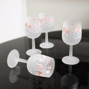 May include: Set of four frosted glass wine glasses with pink and white floral designs. The glasses have a delicate stem and a round bowl.