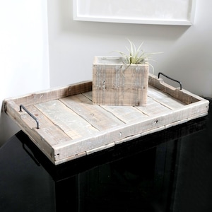 May include: A rustic wooden tray with black metal handles. The tray is made of reclaimed wood and has a natural, weathered finish. A small wooden planter with a green plant sits on top of the tray.