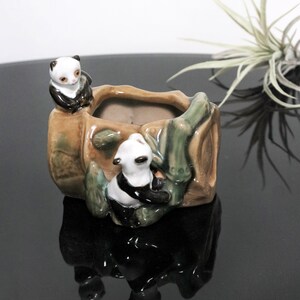 May include: A ceramic planter shaped like a bamboo tree with two panda bears climbing on it. The planter is brown, green, and white.